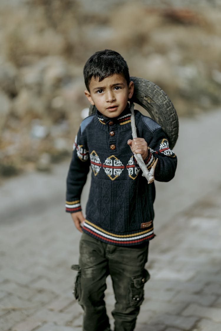 A Little Boy Walking With A Tyre On A Stick 