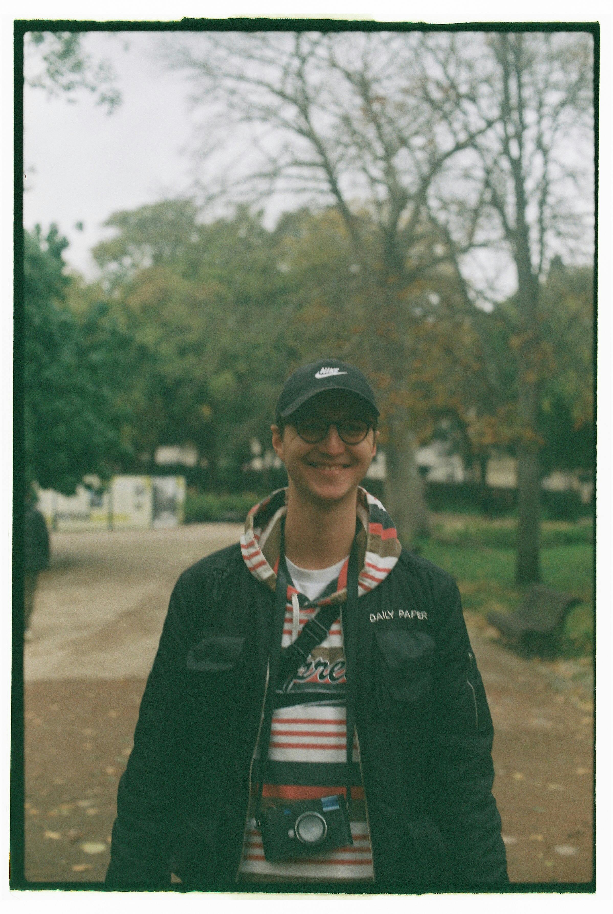 Portrait of a smiling man wearing a cap and glasses in a Lisbon park.