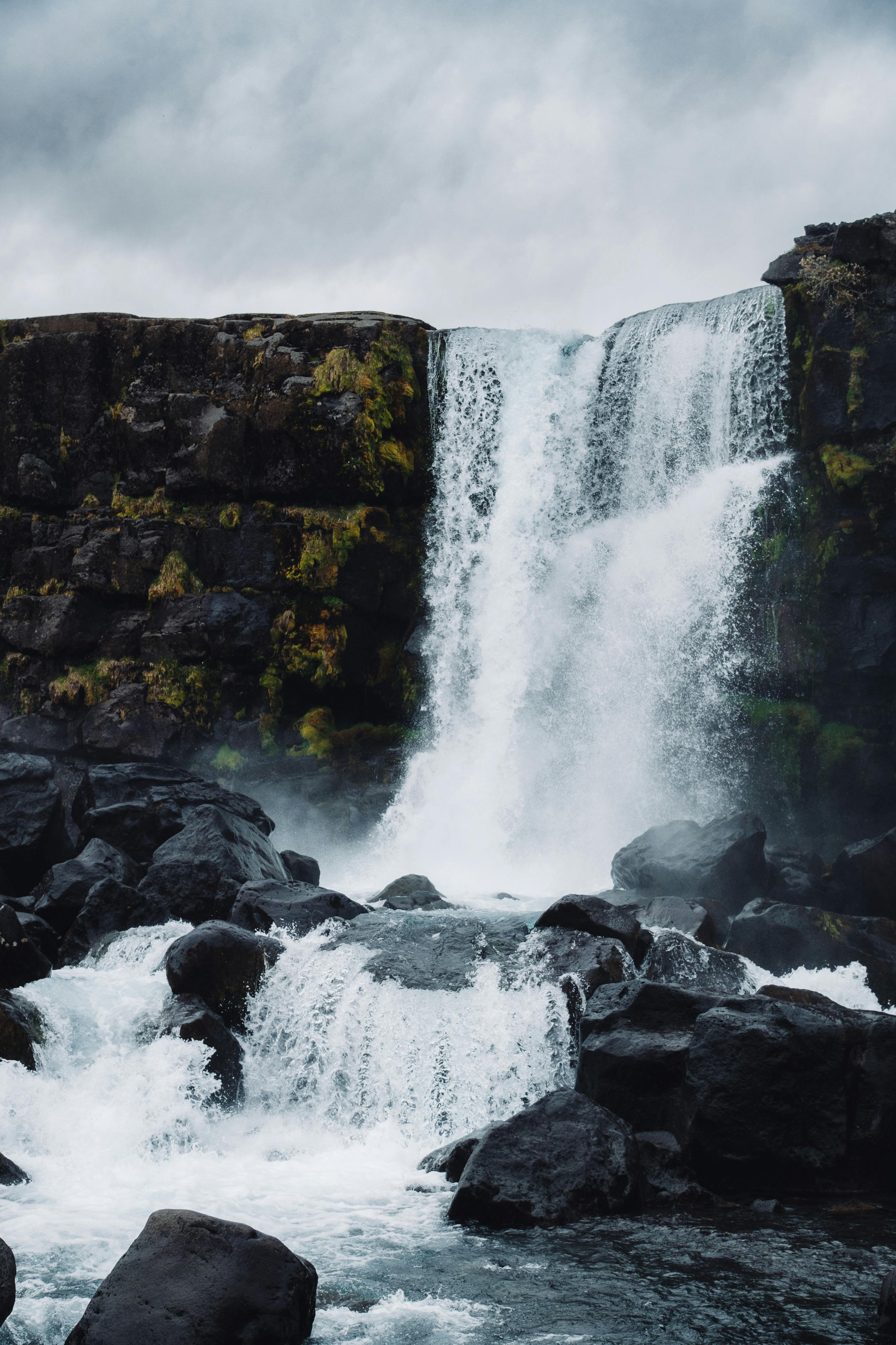 Powerful waterfall cascading over dark rocks with cloudy sky.