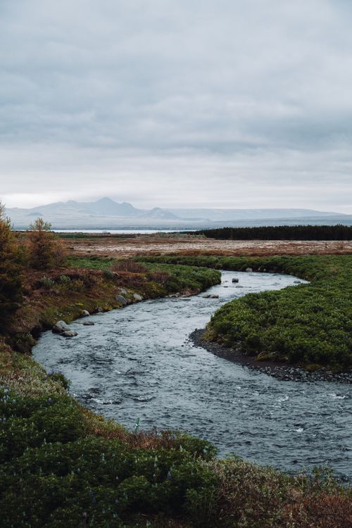 Free A serene river winding through a lush countryside under an overcast sky. Stock Photo