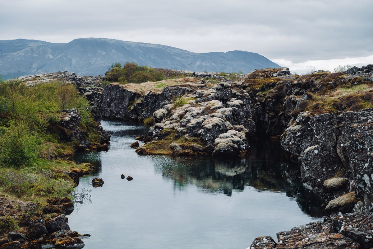 Narrow water-filled fissure canyon at Flosagjá, clear still water reflecting the rock walls and distant mountains.