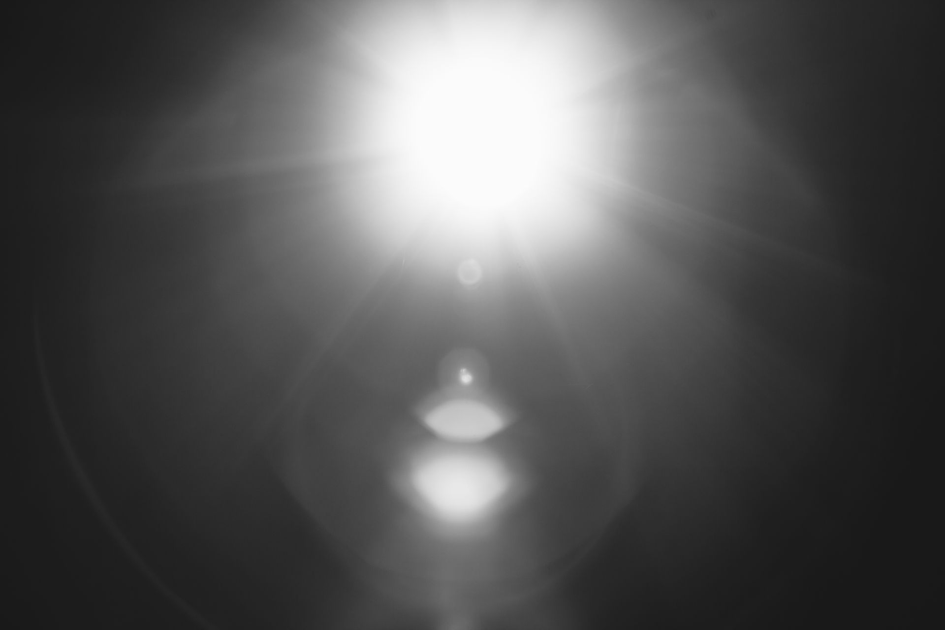 Abstract black and white image of a bright sun flare with lens effects.