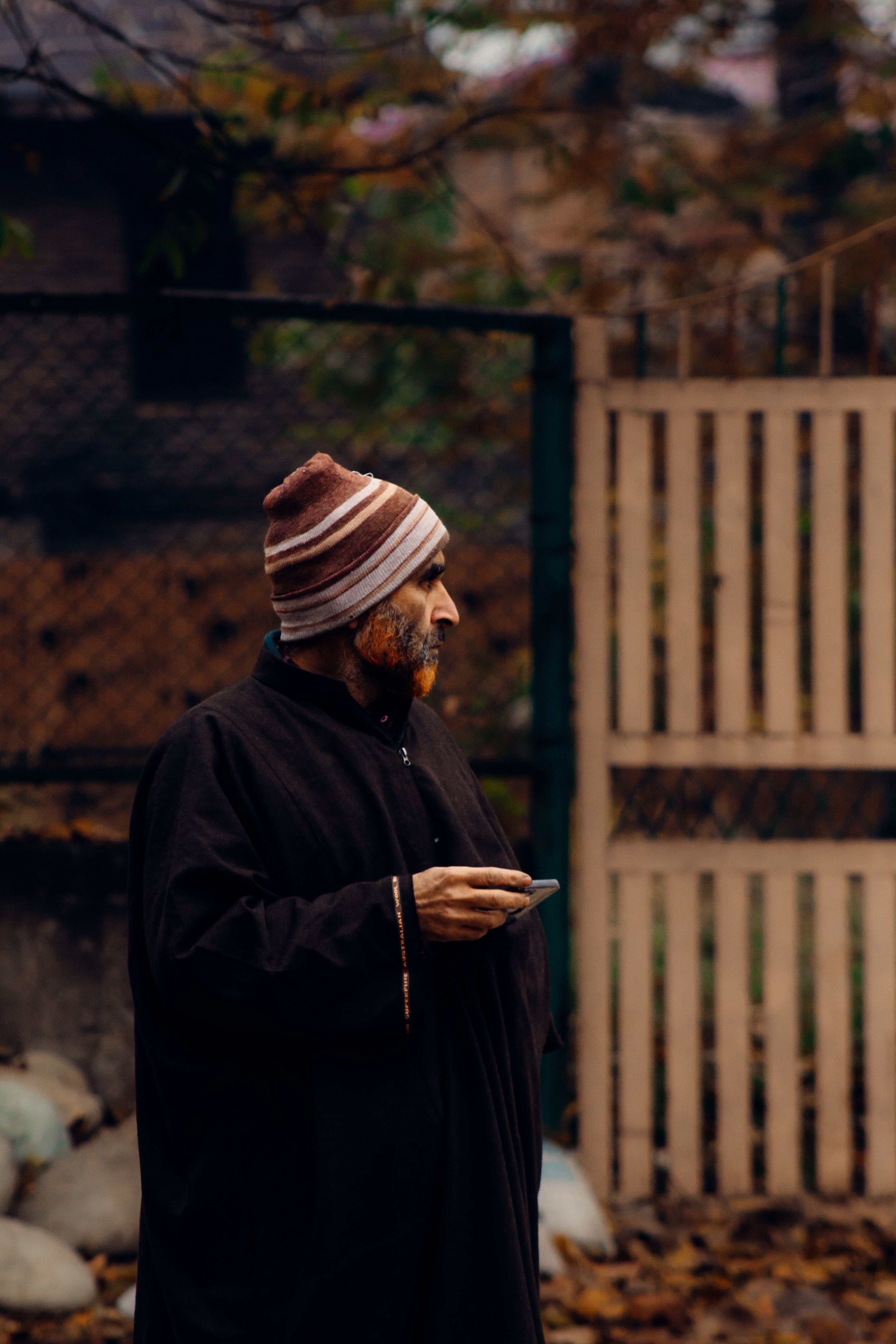 A man in traditional attire stands outdoors holding a smartphone, capturing a serene moment in Jammu.