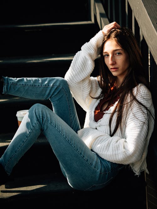 Woman posing on stairs wearing blue jeans and whit sweater 