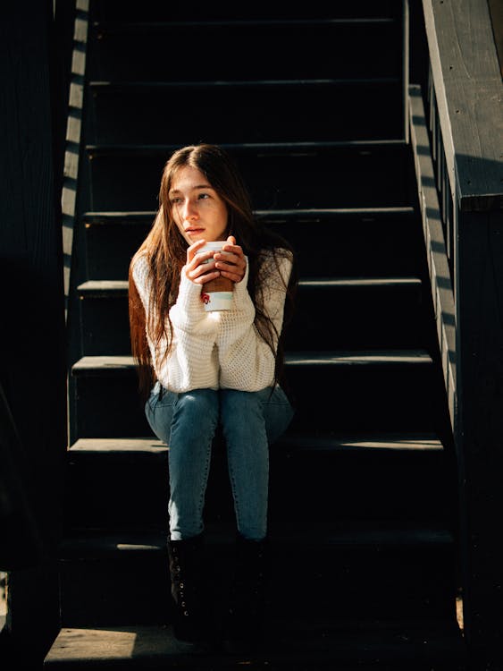 Young woman sitting on stairs drinking coffees 