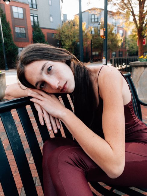 Stylish woman in burgundy outfit sitting on bench in city.