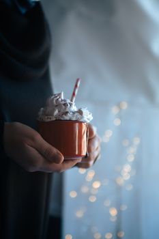 Cozy hands holding a hot chocolate with whipped cream, perfect for winter celebrations.