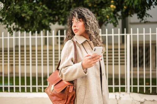 Woman in Coat Standing with Bag and Smartphone