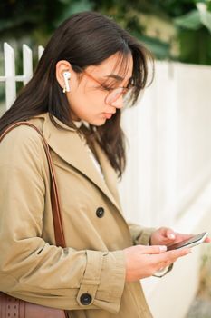 Fashionable young woman using smartphone and earphones outdoors.