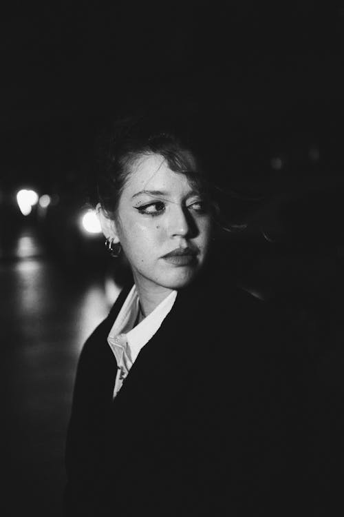 Black and White Shot of a Young Woman Standing Outside in the Dark and Looking Away 