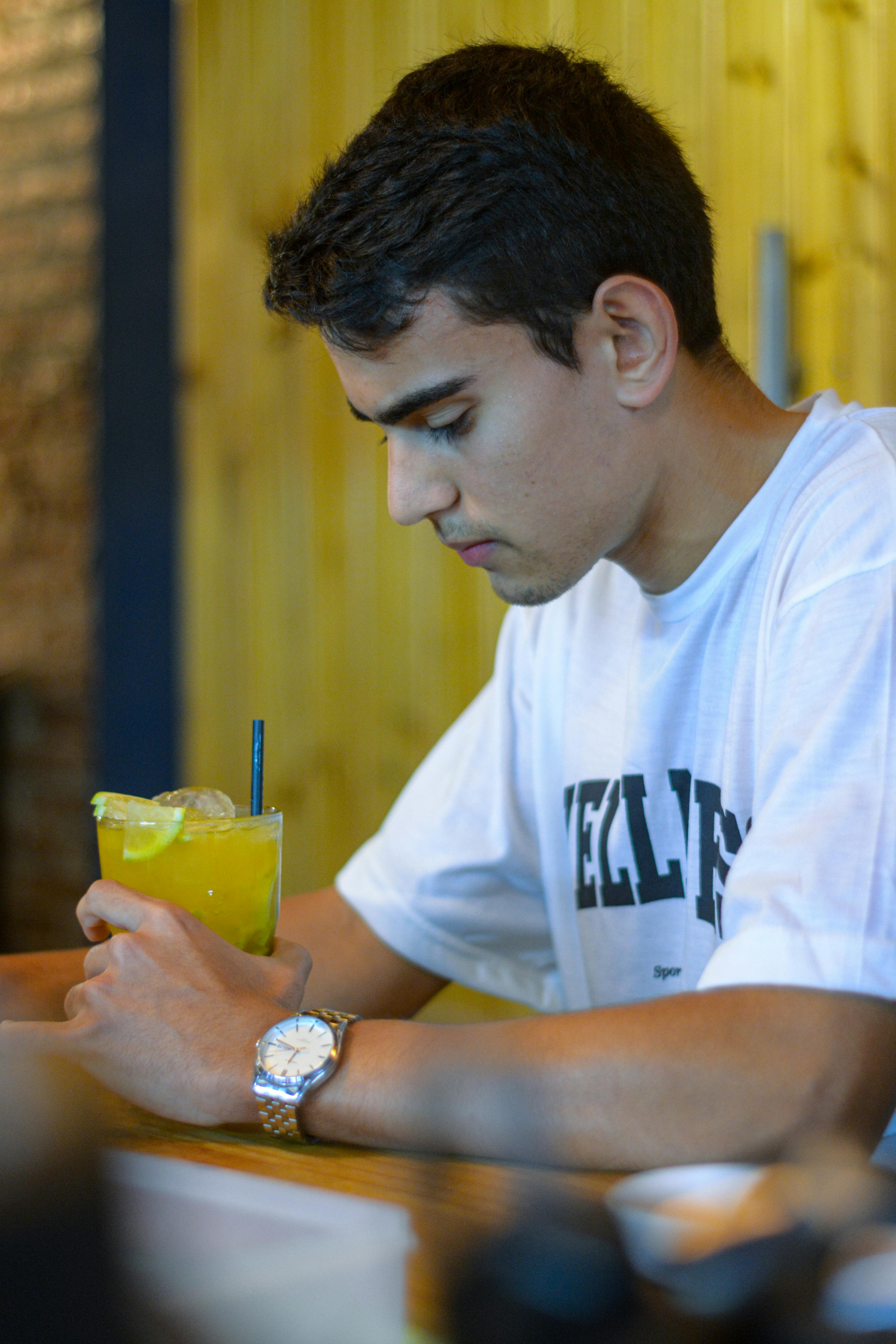 Young man in a café enjoying a refreshing drink with a straw, wearing a white t-shirt.