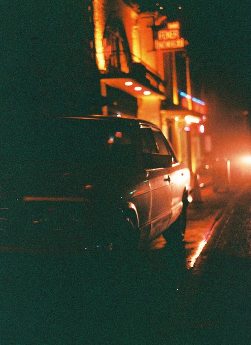 Free A dark city street illuminated by neon lights with a silhouette of a parked car. Stock Photo