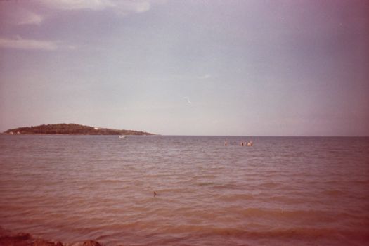 A serene vintage beach scene with people in the ocean under a clear sky.