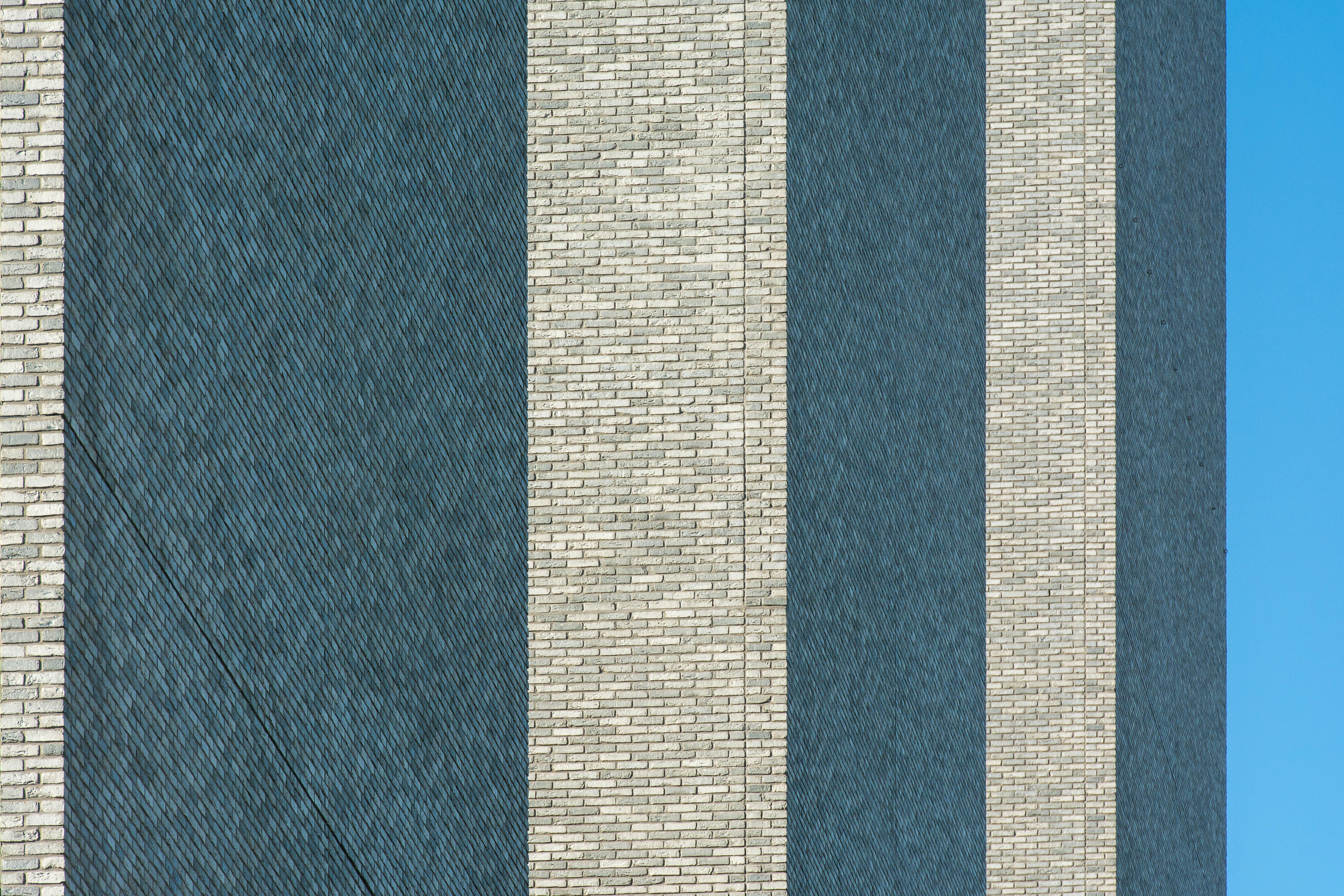 Free Close-up of a modern facade with alternating brick stripes against a blue sky. Stock Photo
