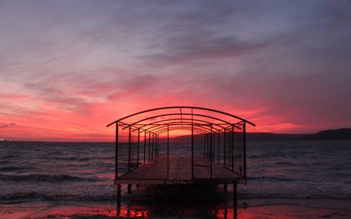 Free Silhouette of a pier extending into the sea with a dramatic sunset backdrop. Stock Photo