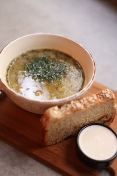 Delicious hearty soup served with bread and a side of cream on a wooden board.