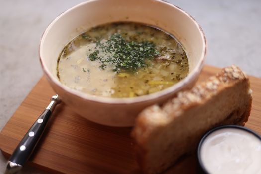 A bowl of delicious chicken soup served with fresh bread on a wooden board.