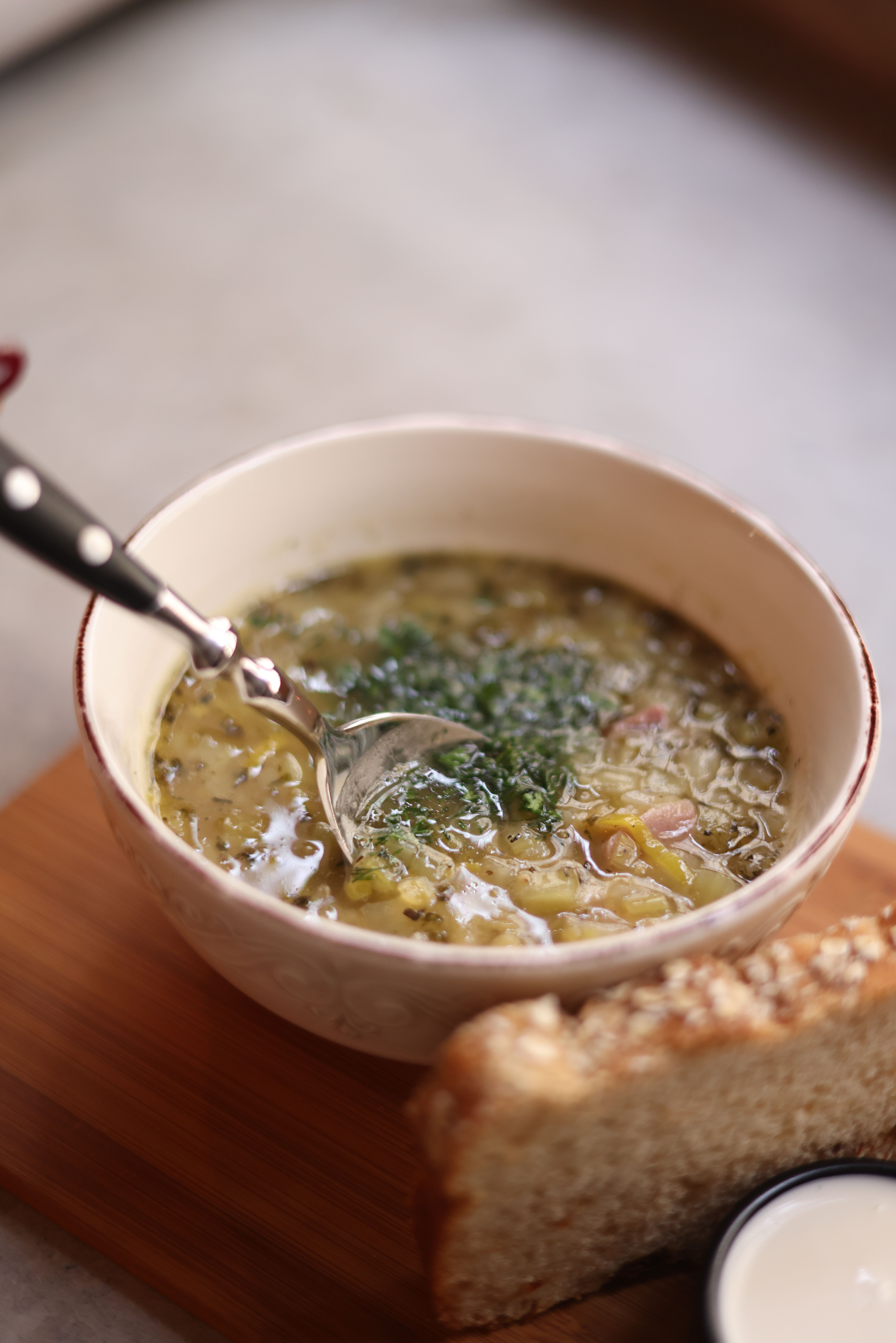 Bowl of delicious vegetable soup garnished with herbs served with bread on a wooden board.