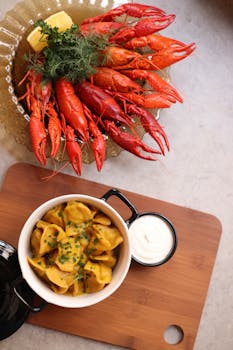 Appetizing seafood platter featuring bright red crayfish, dumplings, and sour cream dip served on a wooden board.