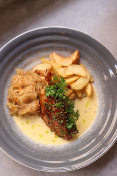 A close-up of a gourmet chicken dish with potatoes and cabbage on a ceramic plate.