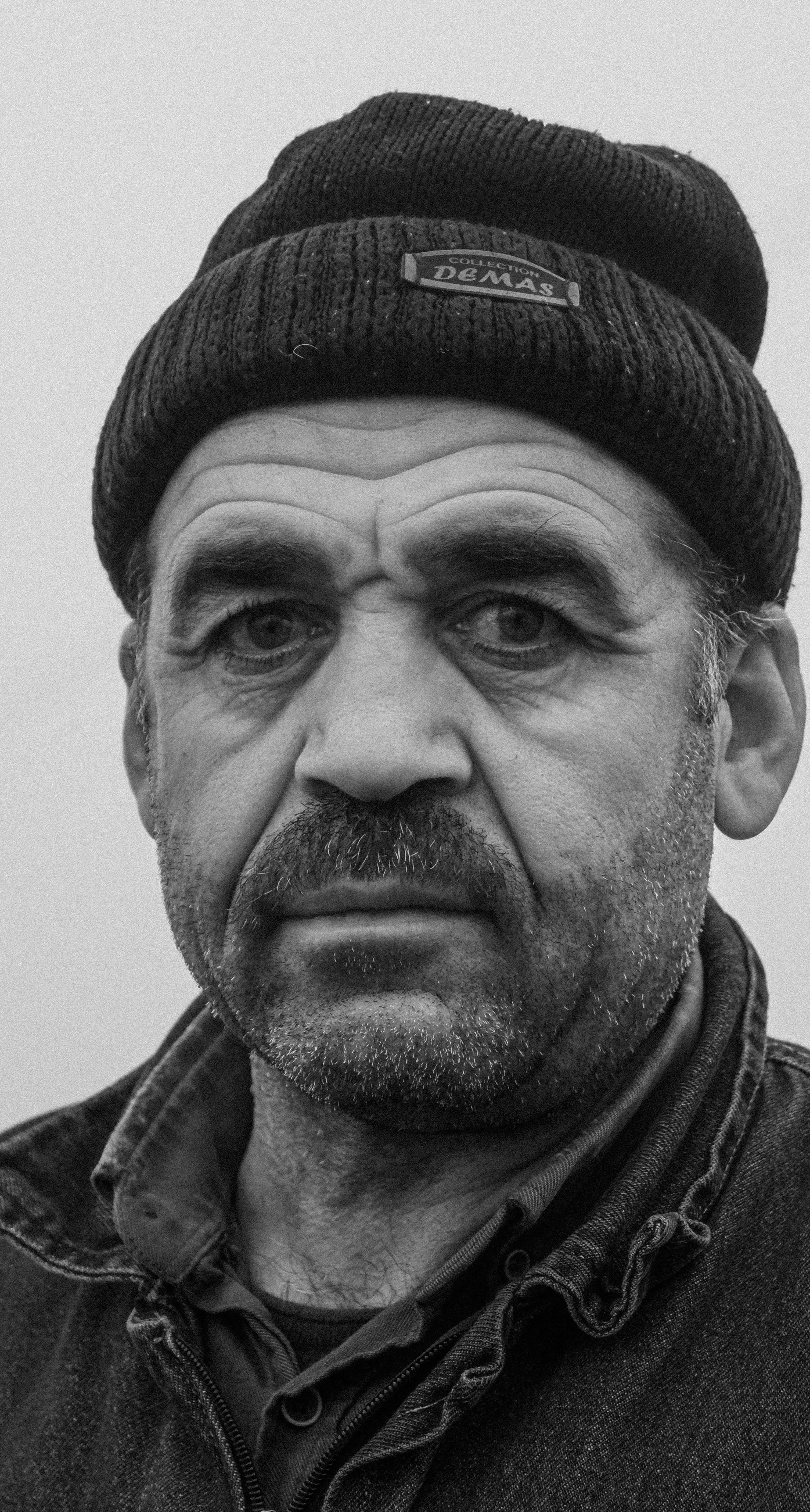 Dramatic black and white portrait of an adult man wearing a beanie with a thoughtful gaze.