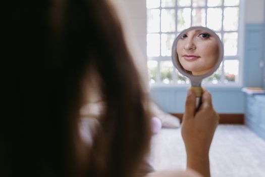 A woman's face reflecting in a hand mirror, captured indoors with soft lighting.