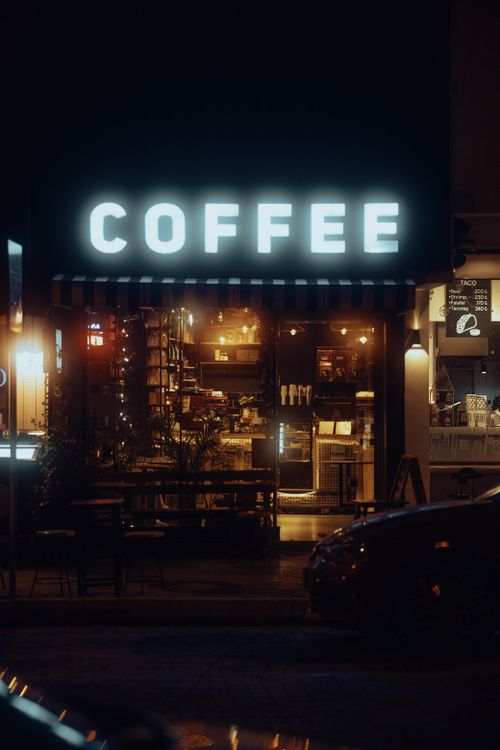 Free Illuminated street view of a cozy urban cafe showcasing a glowing coffee sign at night. Stock Photo