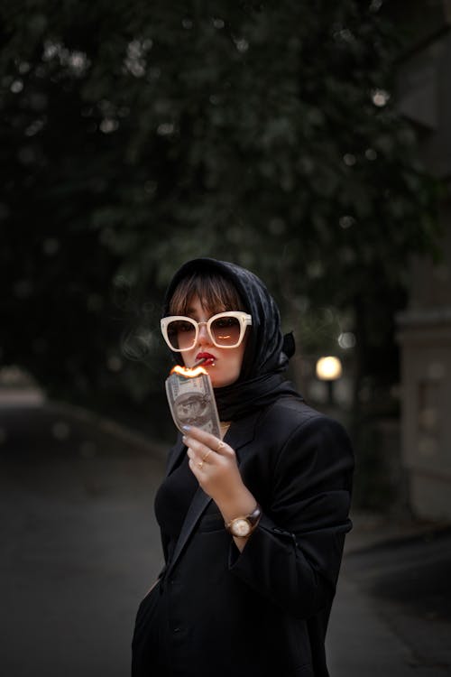 Woman in Hijab and Sunglasses Smoking and Burning Dollar
