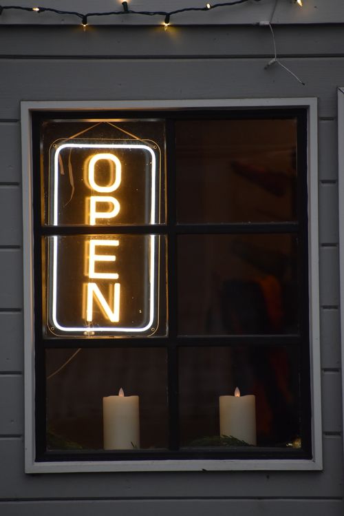 Free A stylish café window featuring a bright neon open sign with decorative candles. Stock Photo