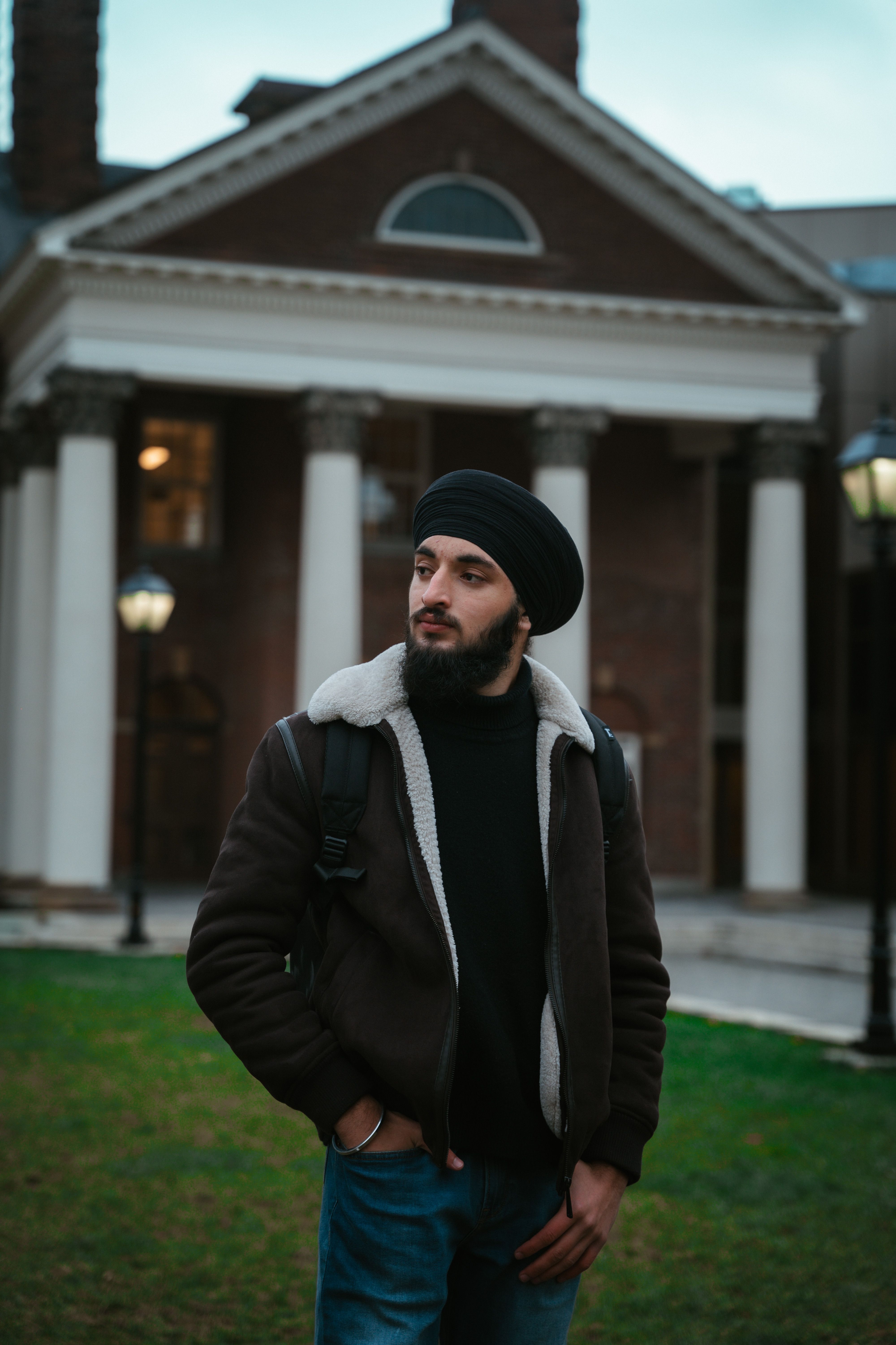 A stylish man with a turban stands confidently outside a historic building with tall columns.