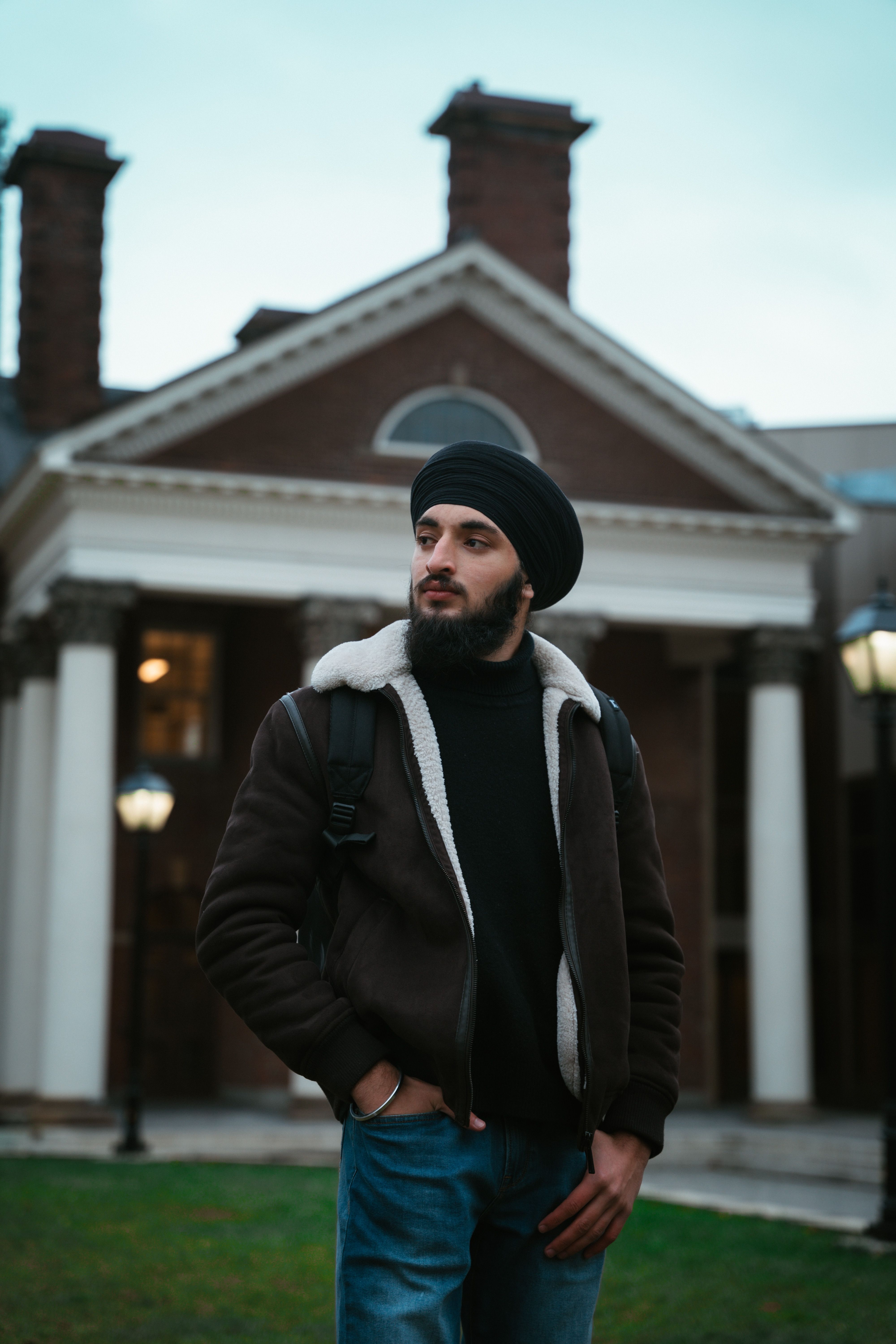 A fashionable man with a turban poses confidently before a historic building.