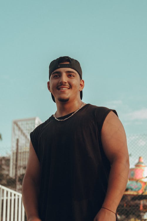 Young Man in a Tank Top and Baseball Cap Standing Outside and Smiling 