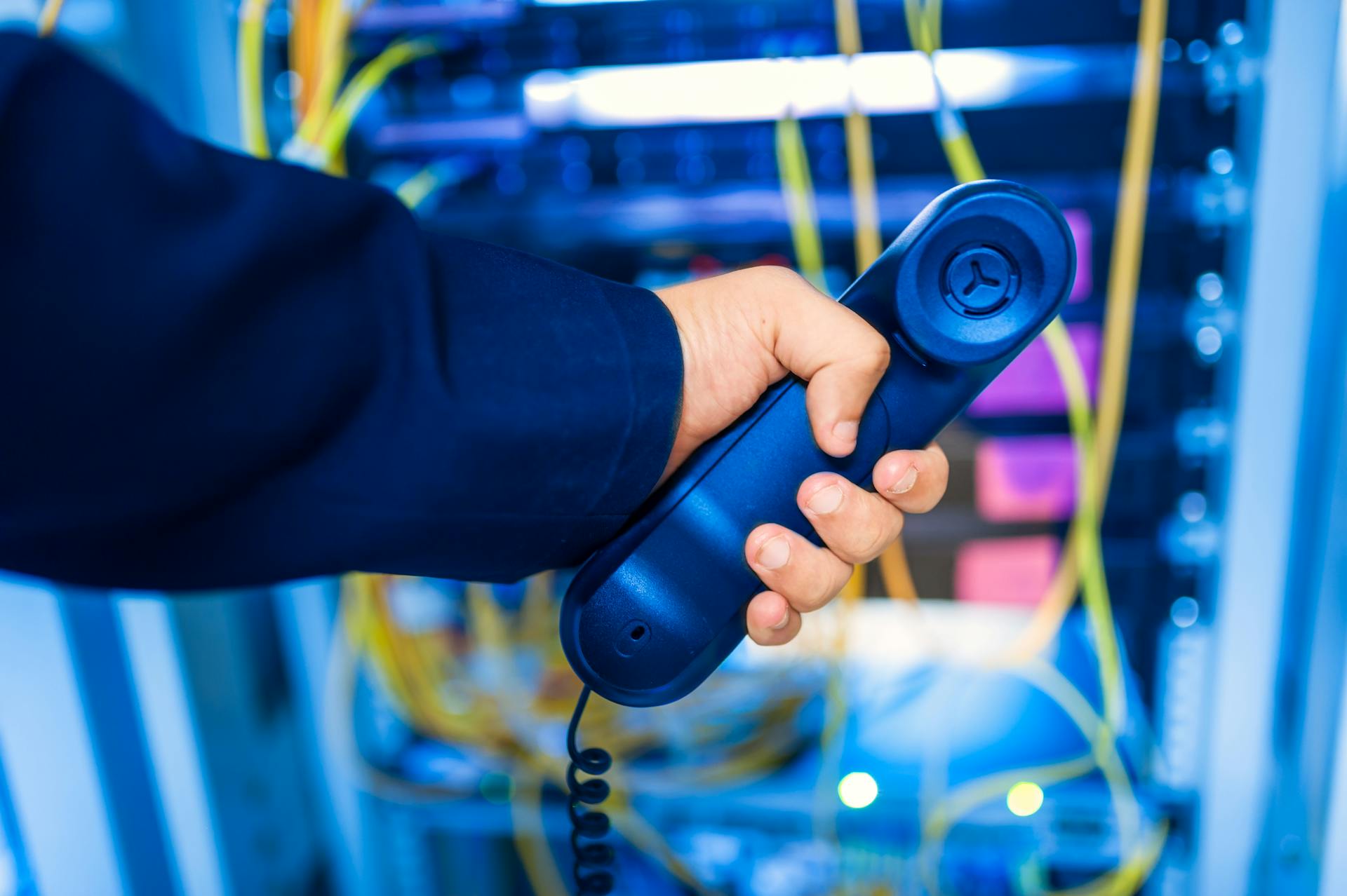 Close-up of a hand holding a telephone receiver in a server room emphasizing technology.