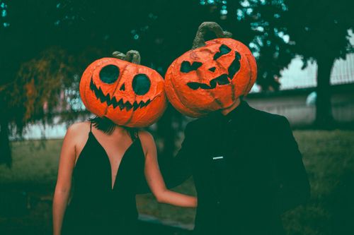 Free A couple in stylish Halloween costumes with pumpkin masks, posing outdoors during fall. Stock Photo