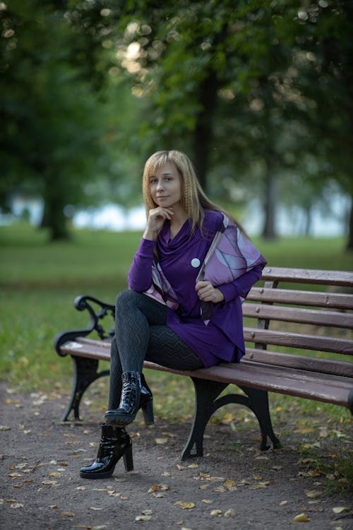 Woman Wearing a Purple Blouse Sitting on a Bench in a Park