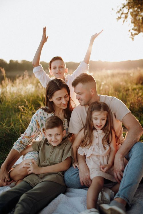 Free A joyful family sitting together outdoors in a sunny meadow, enjoying quality time. Stock Photo