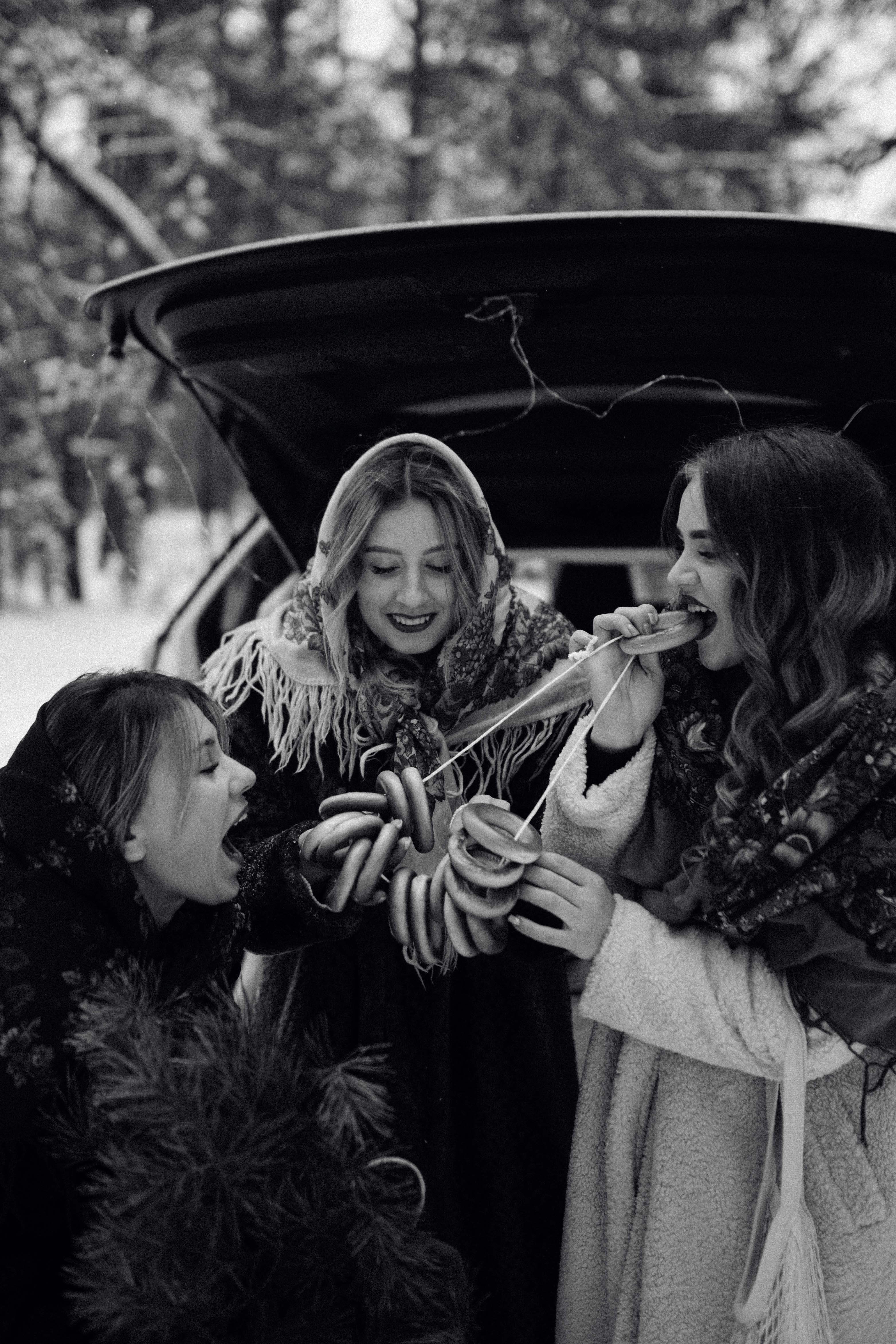 Three women sharing traditional pastries outdoors, enjoying a winter celebration.