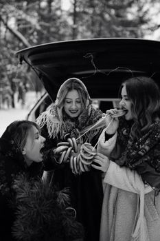 Three women sharing traditional pastries outdoors, enjoying a winter celebration.