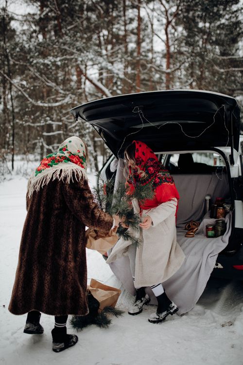 Free Two women in winter clothing unloading a car trunk in a snowy forest setting. Stock Photo