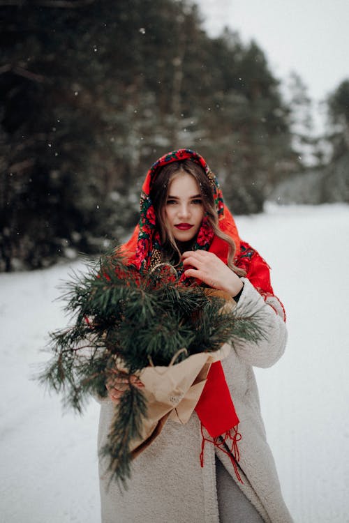 Woman in Coat and with Evergreen Leaves in Winter