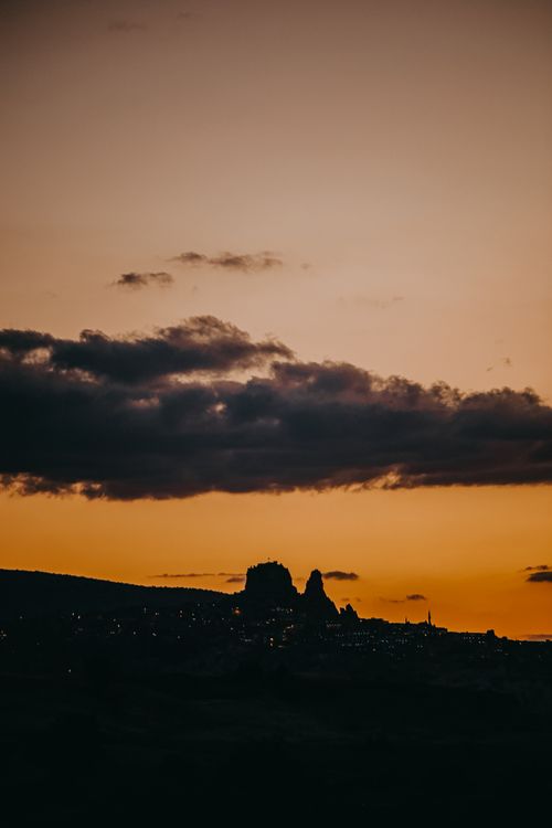 Free A city skyline silhouetted against a vibrant evening sky with clouds and distant lights. Stock Photo