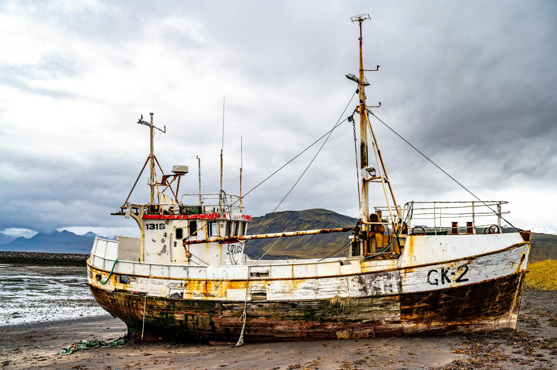 A weathered shipwreck on a tranquil beach beneath cloudy skies, highlighting nature's reclaim.