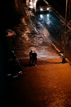 Couple walking under an umbrella on wet city streets at night.