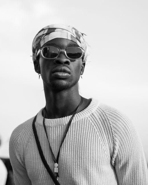 Black and white portrait of a young man with headscarf and sunglasses, exuding fashion and style.
