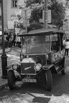 Black and white photo of a vintage car parked in a city street with pedestrians.