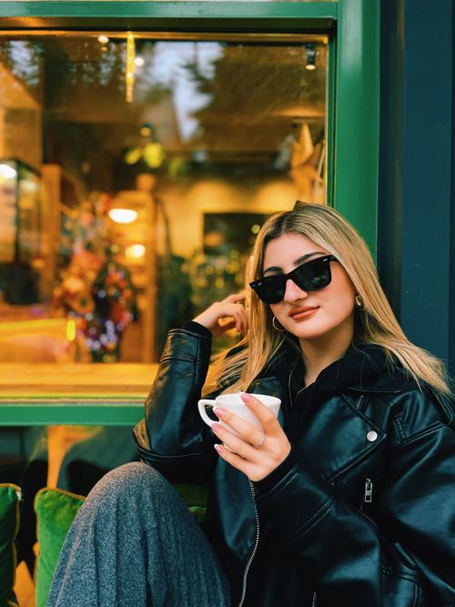 Free Woman in sunglasses savoring coffee outside a cozy café with vibrant Christmas decor. Stock Photo