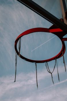 A rusty basketball hoop with a plane contrail in the clear blue sky, resembling a dynamic outdoor setup.