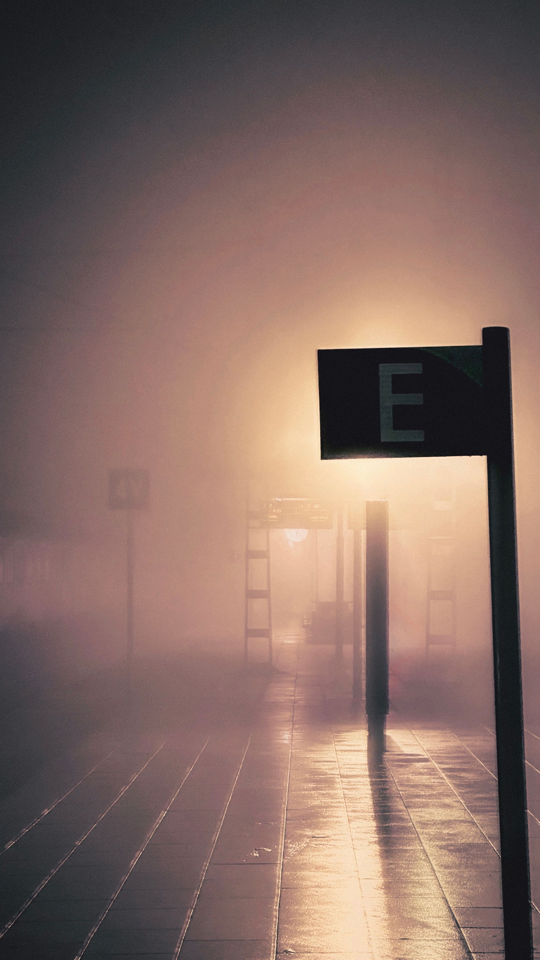 A foggy night view of an empty Casablanca train station with illuminated signs and wet pavement.