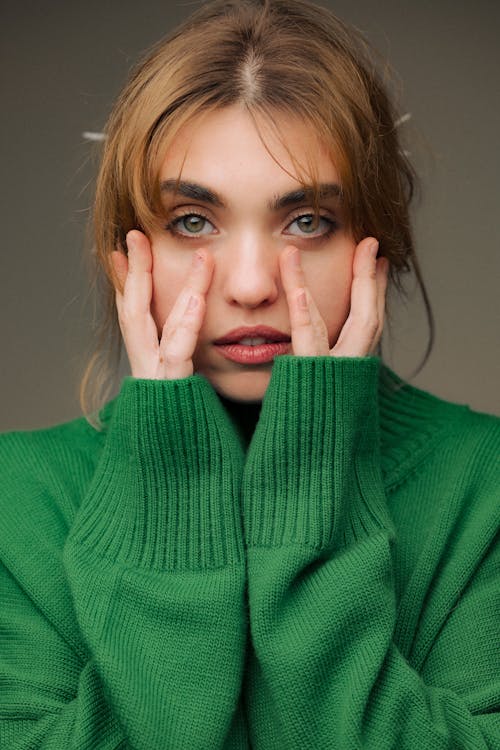 Young Woman in a Green Wool Sweater Touching Her Cheeks
