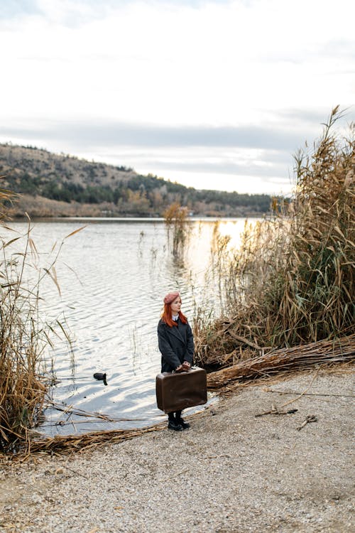 Redhead Woman with Suitcase on Riverbank